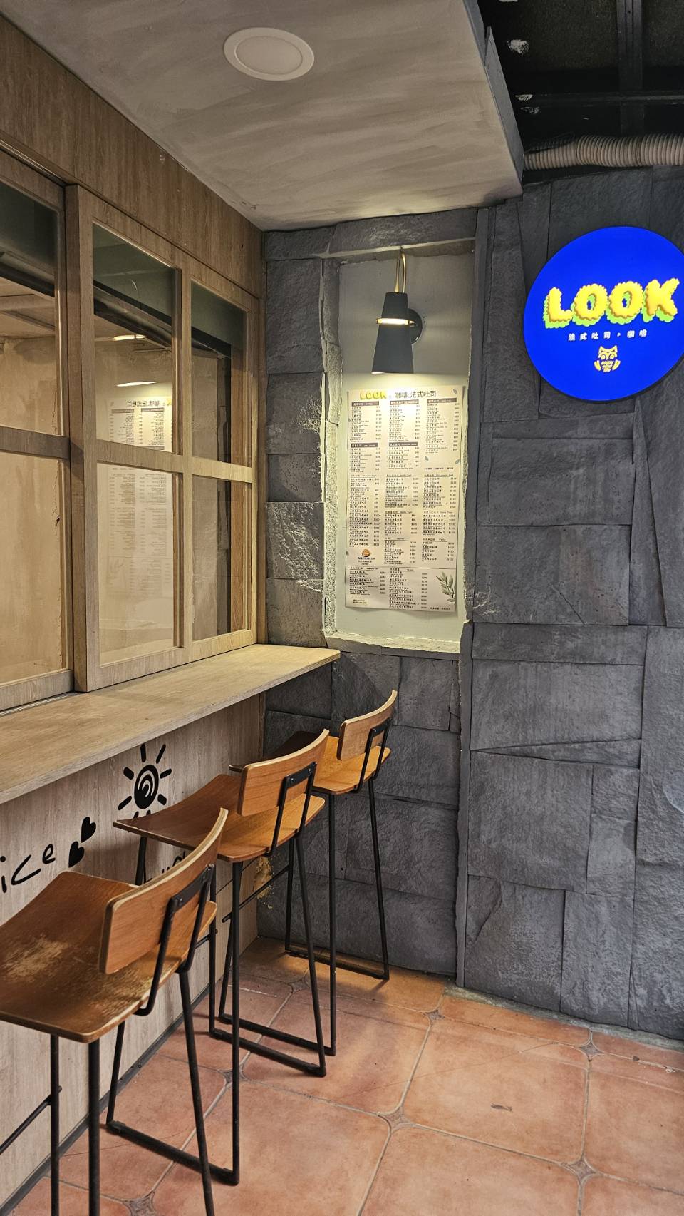 Look Café 店內吧檯座位區，木質高腳椅、清水模牆面與 LOOK 藍色霓虹招牌